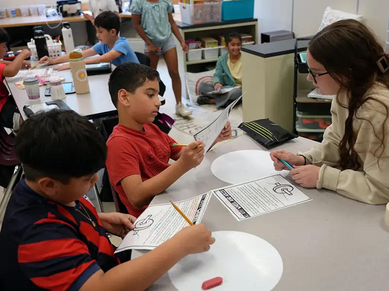 adult sitting at a table with two students working