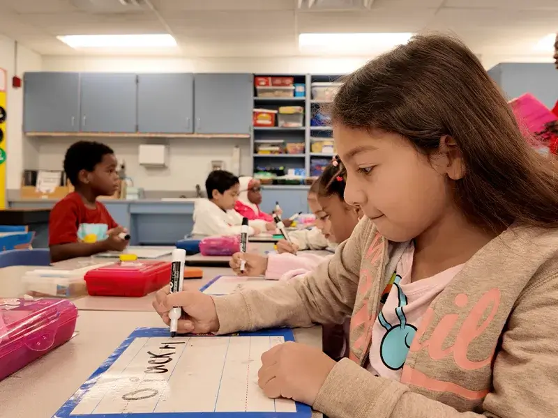 Elementary school student on a white board while seated in a classroom