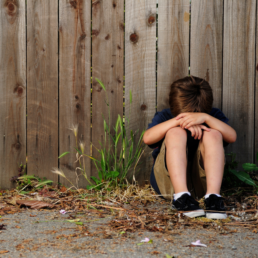 photo of boy sitting by a fence with head cradled in arms