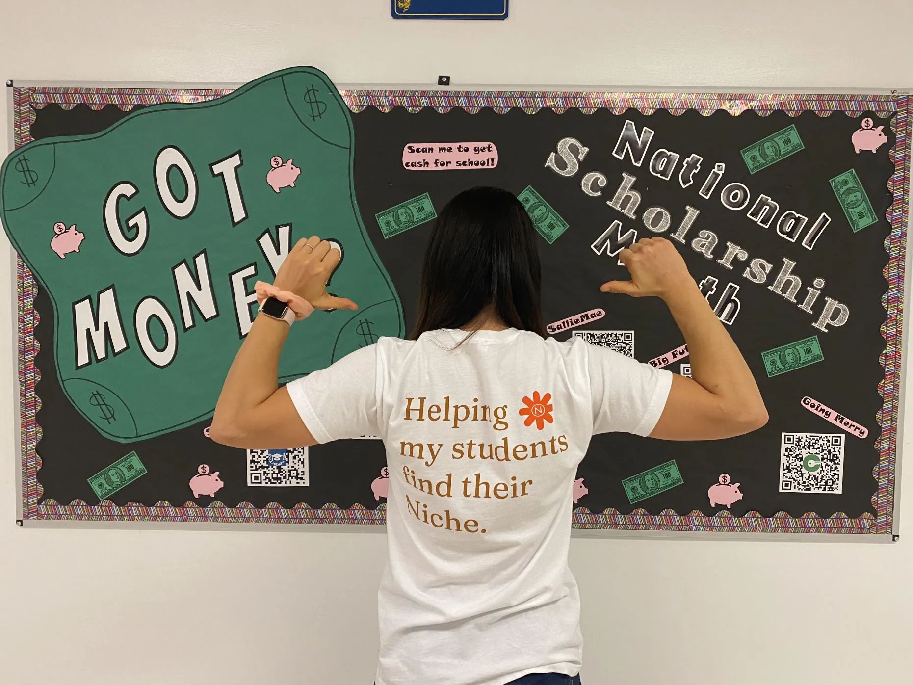 Collage and Career Counselor promoting scholarships in front of scholarship bulletin board.  Counselor is facing bulletin board and back of t-shirt reads: Helping my students find their niche.