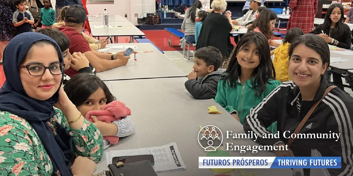 Springwoods Elementary School cafeteria with people and tables, several children and two mothers are smiling at the camera as they sit at the nearest table