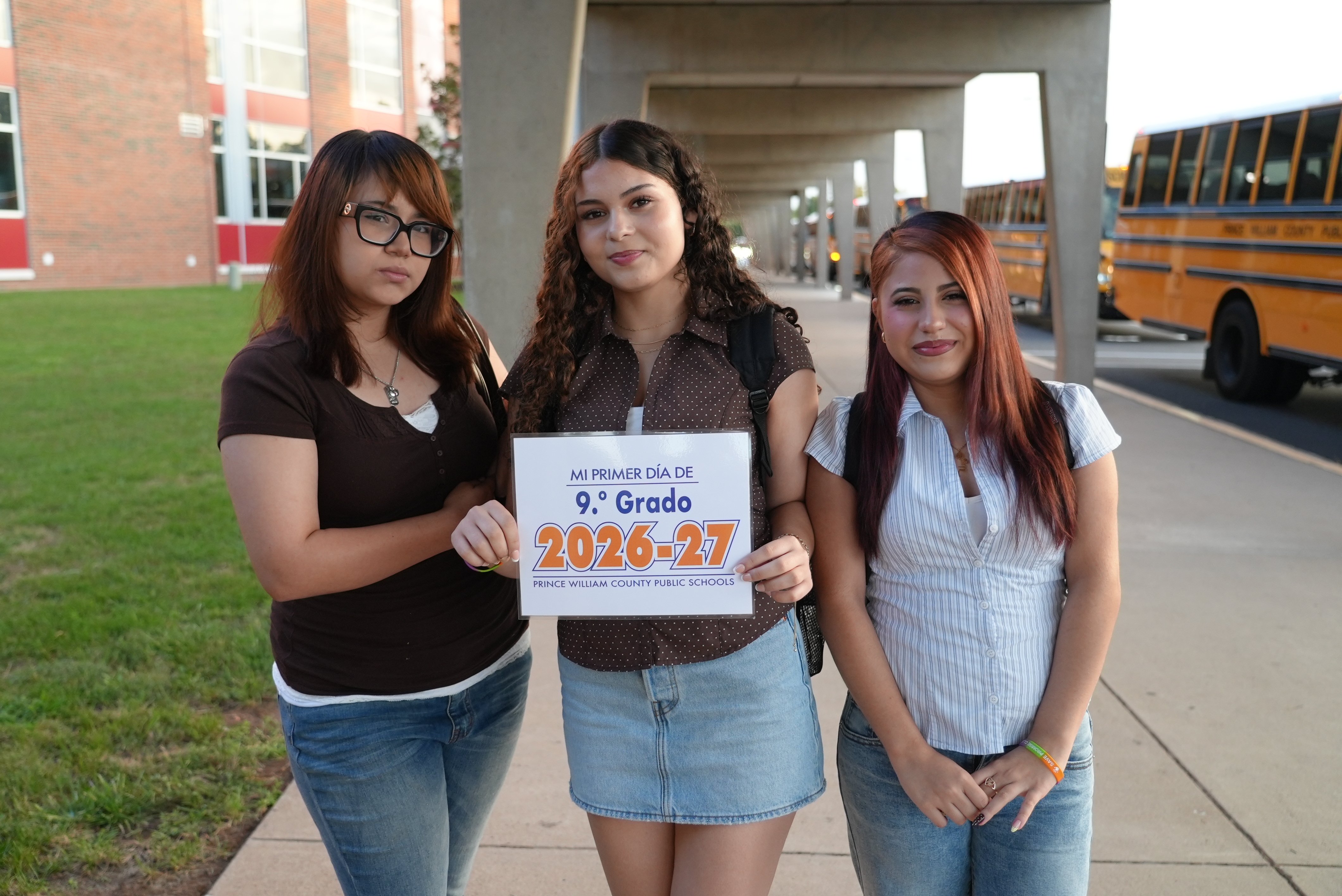 Three students smile at the camera in the front of their school