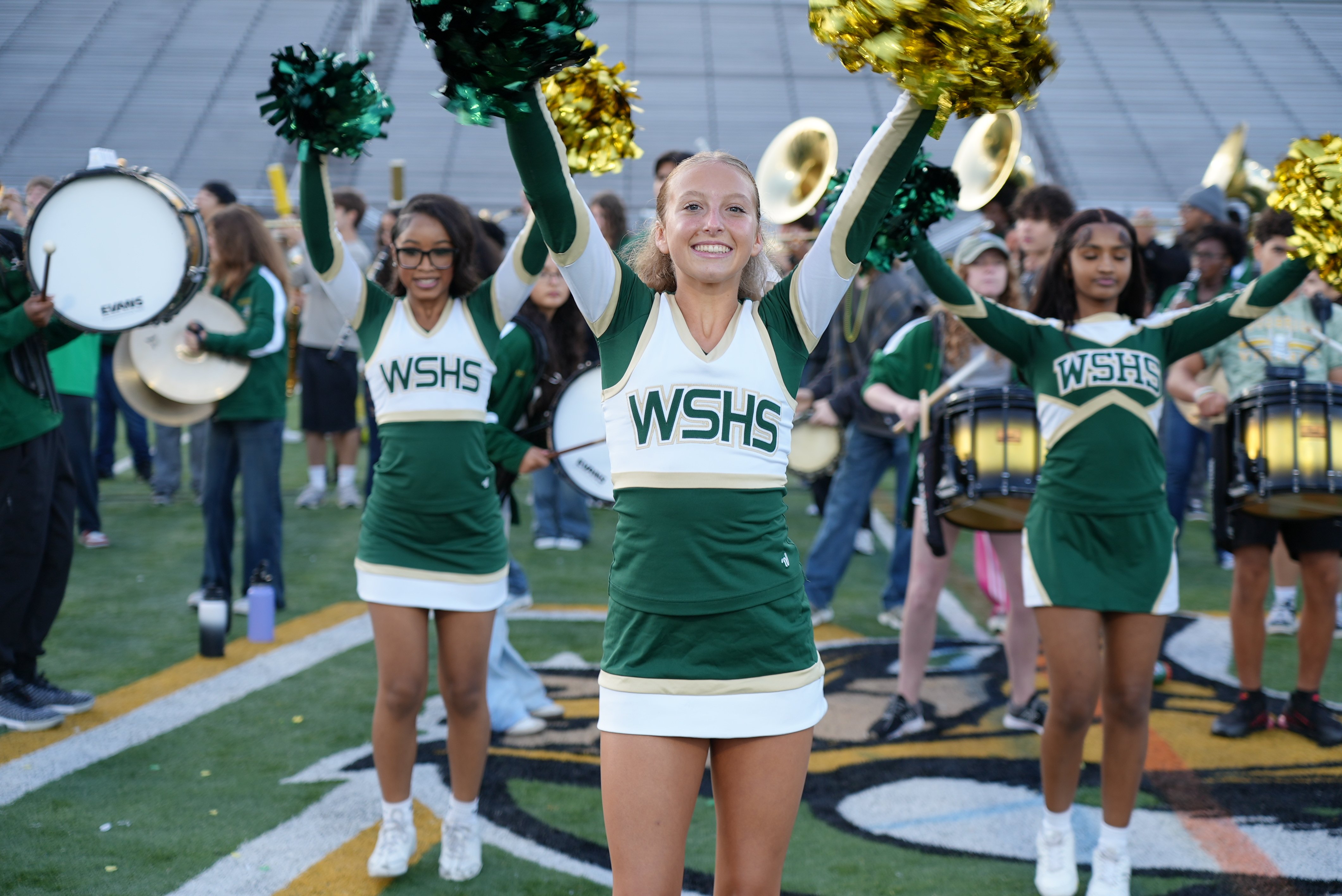 Three Woodbridge High School cheerleaders cheer during a morning pep rally on the football field.