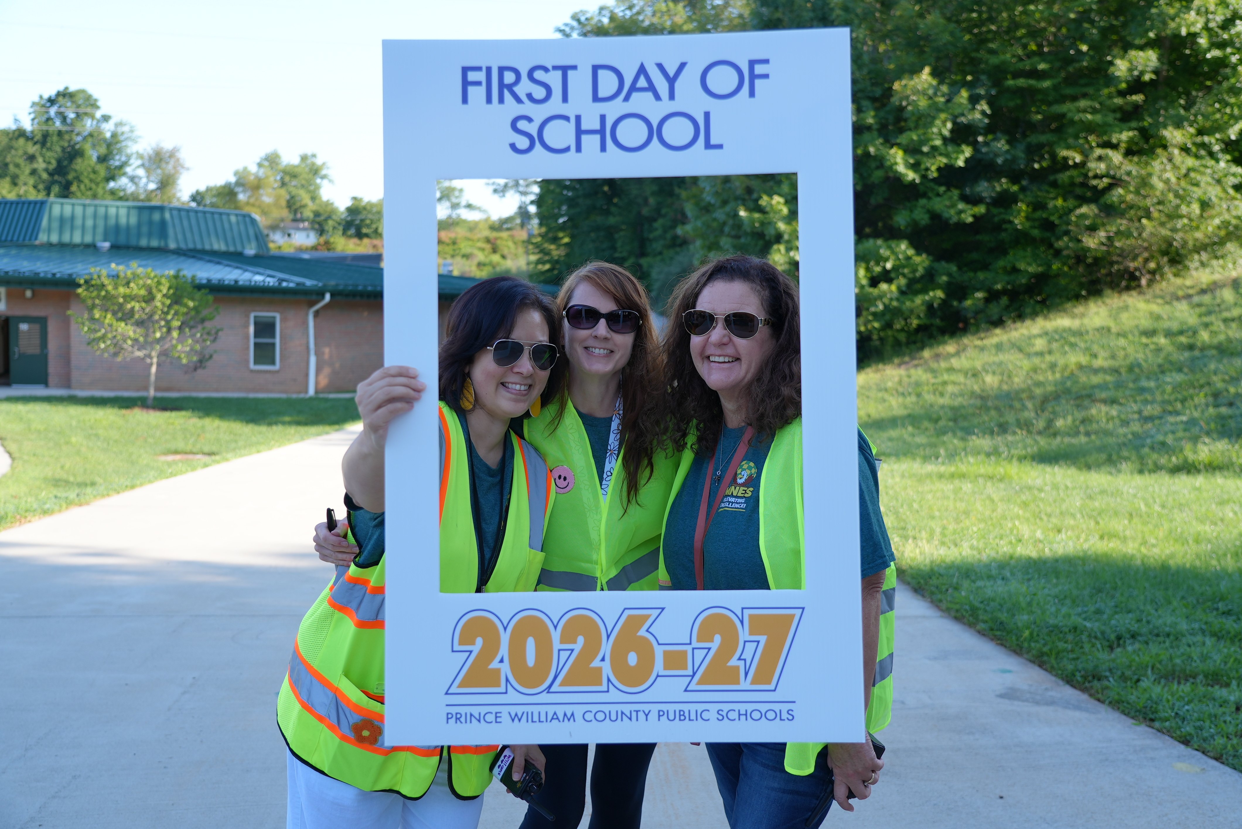 Three staff members hold a first day of school portait up