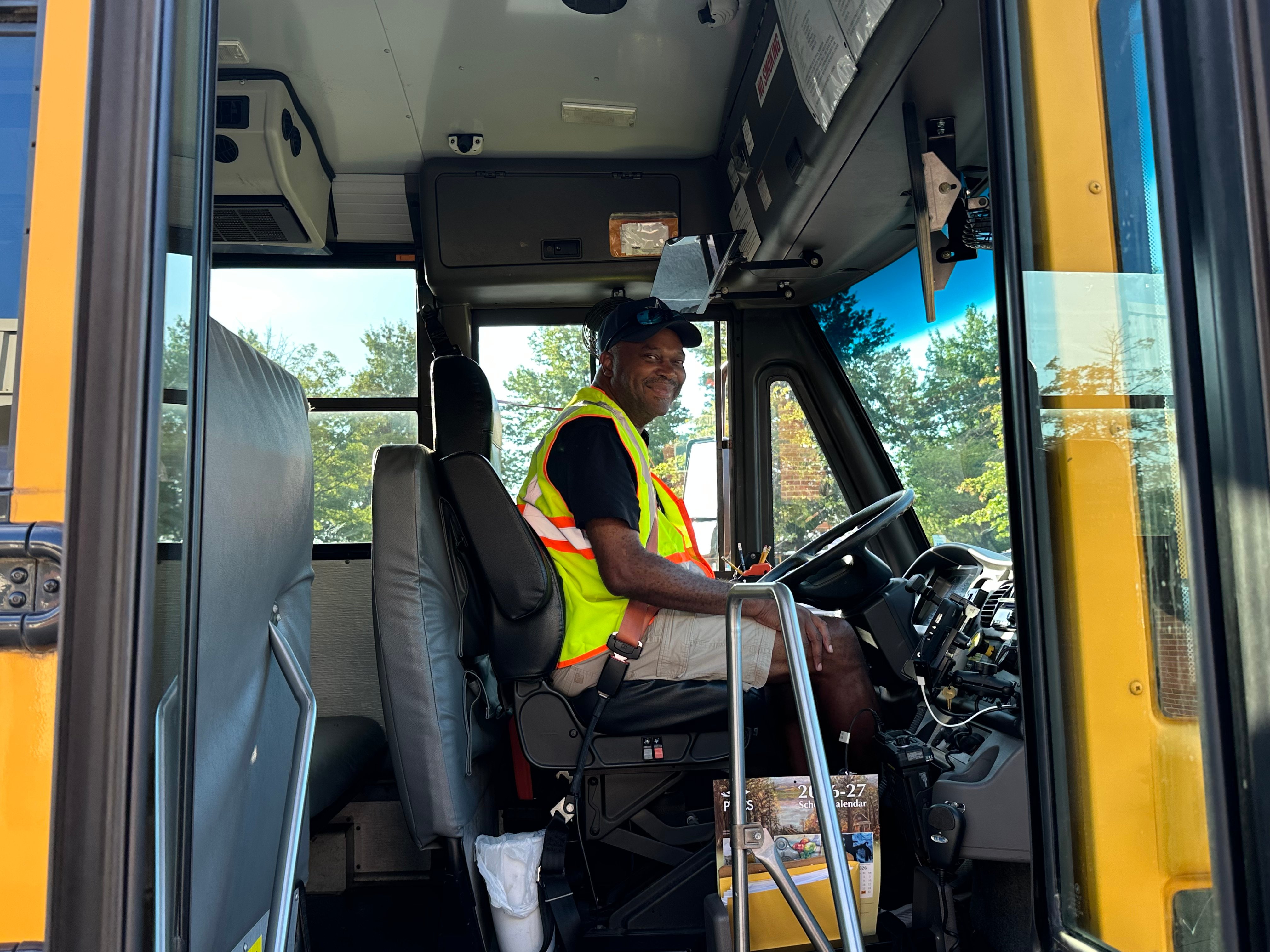 A bus driver smiles while sitting in his seat