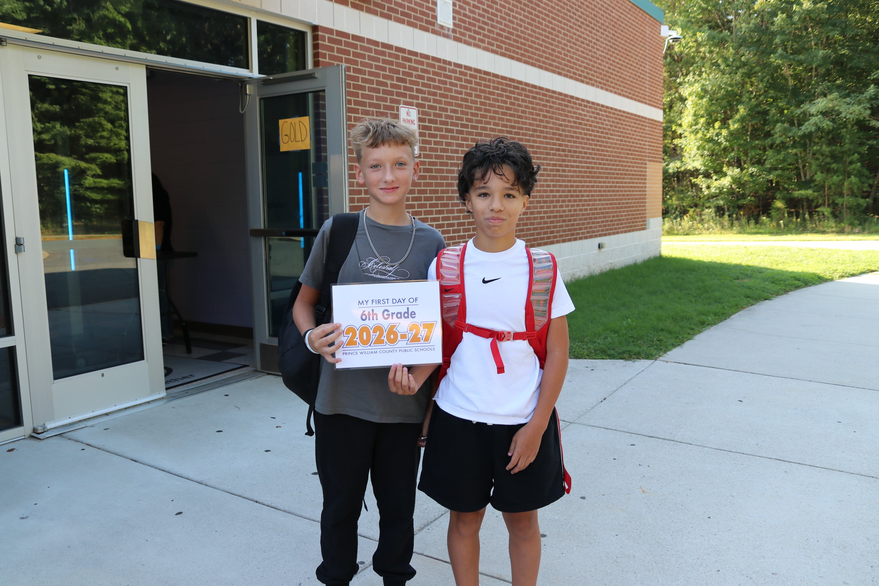 Two students smile at the camera while holding a first day of sixth grade sign