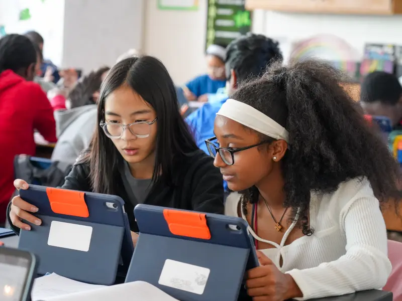 Middle school students working together and looking at an iPad