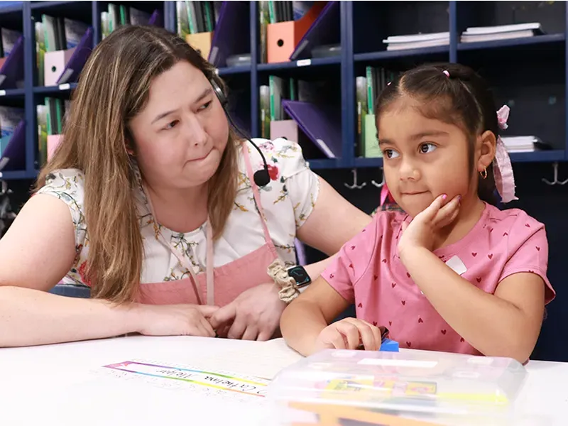 Elementary school teacher and student sitting at a table in a classroom