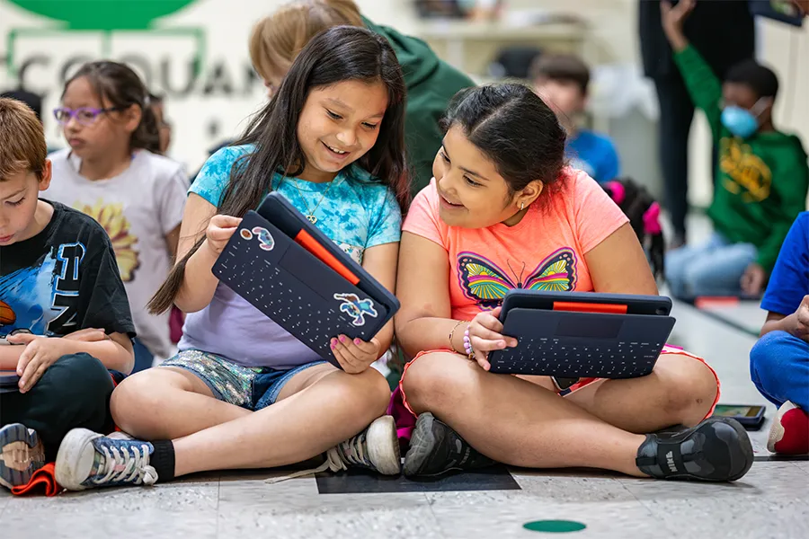 Elementary school students sharing their work with each other on their iPads while seated on the floor