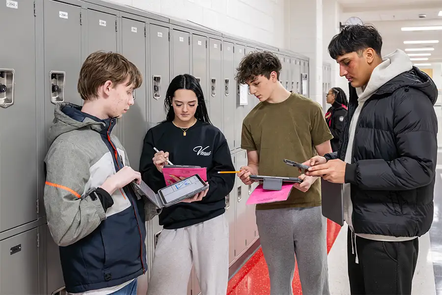 Students with iPads near lockers in a hallway