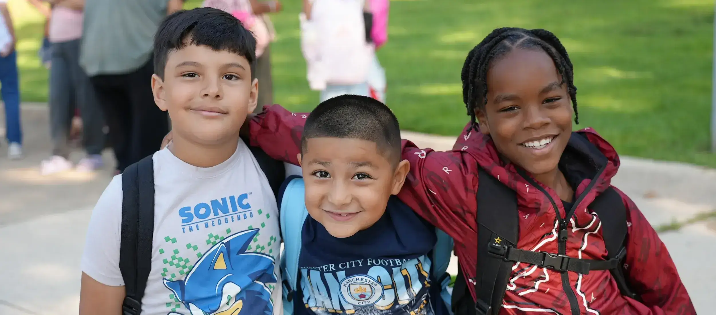 Three elementary school students posing for photo outside the school on the first day of school