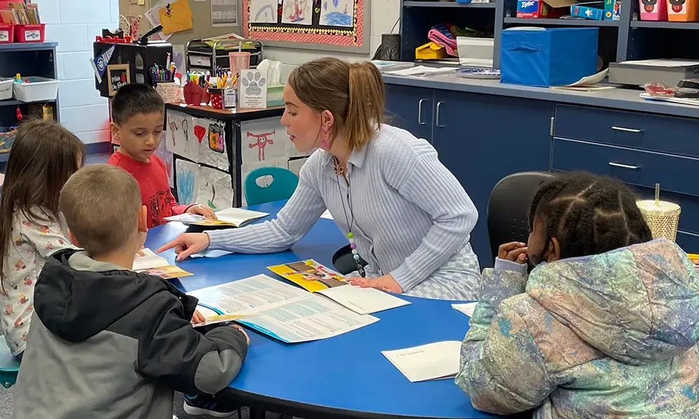 Teacher sitting in an elementary school classroom with a diverse group of four students