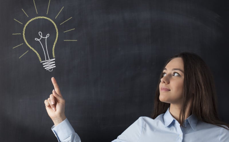 Teacher standing in front of a blackboard with an illustration of a light bulb written in chalk