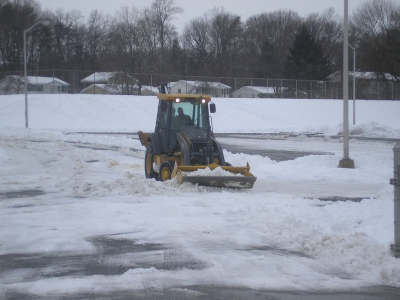 Snow plow clearing a school parking lot.