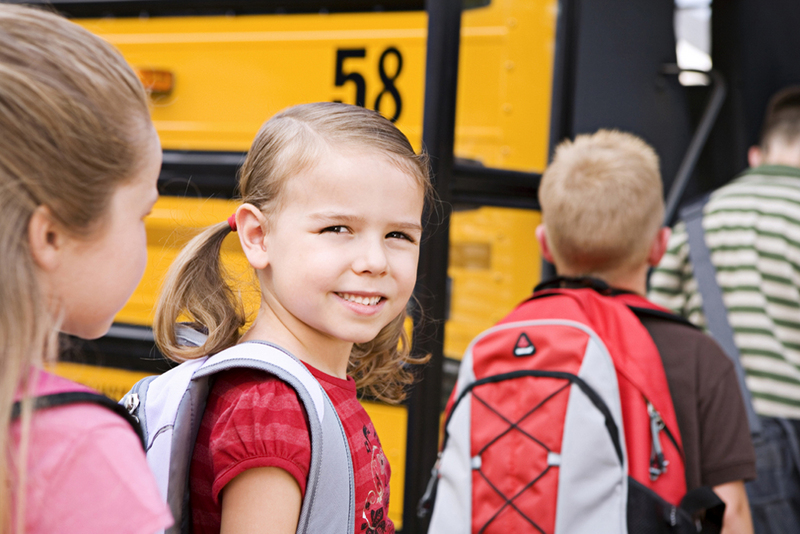 Smiling girl preparing to board a school bus.