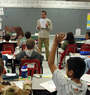 Teacher holding a sheet of paper standing in front of a classroom full of students