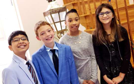 (left to right are Muhammad Saifullah Usufzai, Braedon Strahley, Aniyah Rush, and Ava Green), dressed up for their competition, elementary students from Haymarket ES debate team standing shoulder to shoulder and smiling