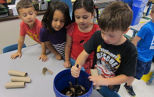 A group of male and female students at Coles Elementary stirring a bucket of compost in their classroom