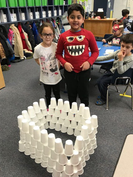 a girl and a boy standing in front of a building made of stacked cups