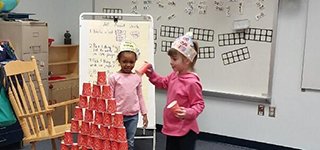 three students standing behind a tower made of stacked cups