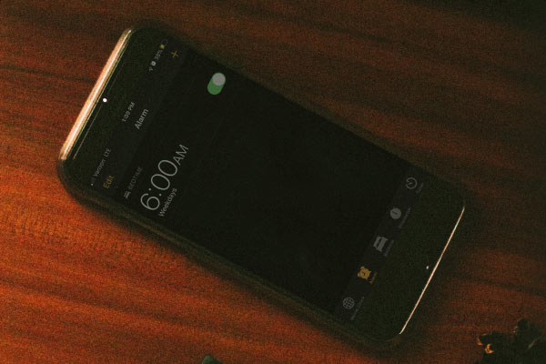 A cellphone on a table with the clock showing 6 a.m. 