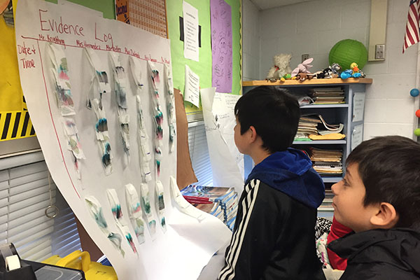 Two students looking at an evidence log poster with individual samples of chromatography on it