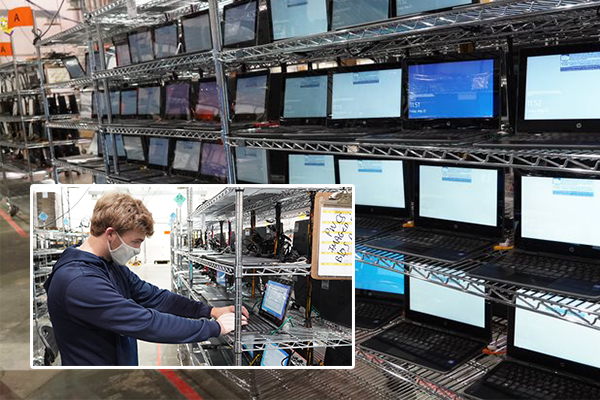 Metal racks filled with open laptops. Man working on one.