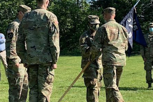 Four individuals in army fatigues one holding a flag.