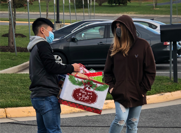 A female student and a male student in a parking lot. Male student holding a gift bag