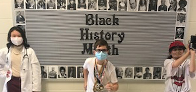 Three students posing in front of bulletin board