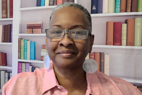 serene photo of April Barrett, reading specialist at River Oaks Elementary, with a soft smile and round dangle sitting in front of a bookcase full of colorful books