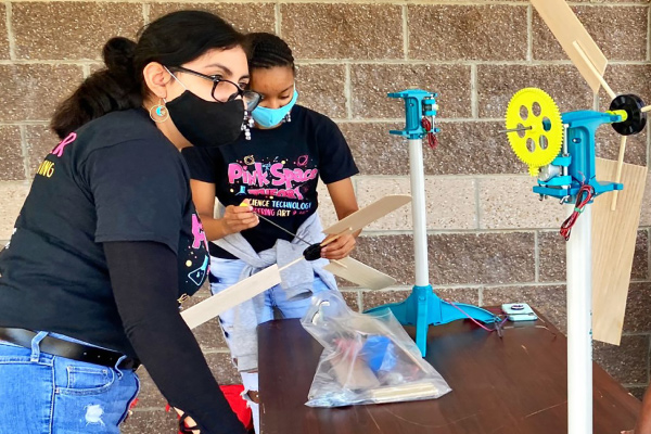 two female students working outside at a table building a windmill