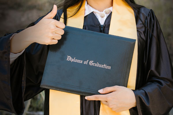 Graduate holding diploma with thumbs up