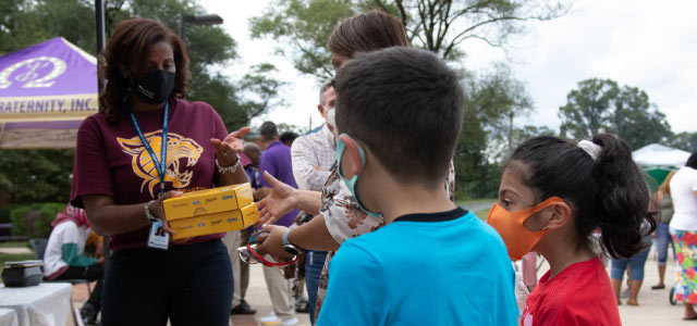 Dr. LaTanya McDade handing out school supplies to two elementary aged children.