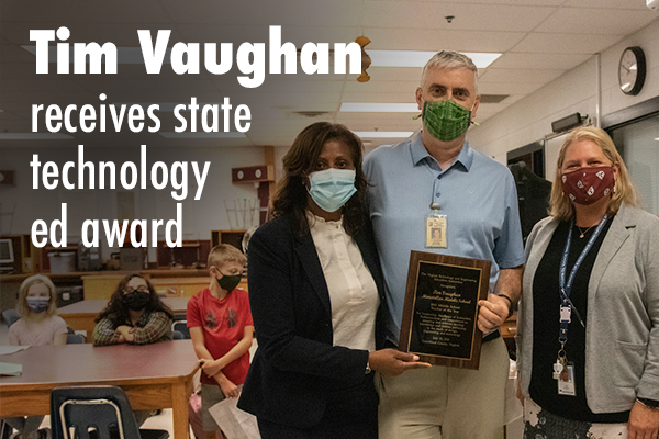 Photo of three individuals in a lighted school area, with (l) Superintendent of Schools Dr. McDade, (c) Tim Vaughan holding a plaque, and (r) Marsteller Principal Lisa Warner