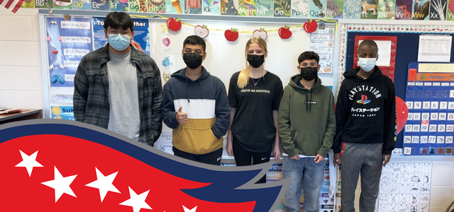 Five Patriot High School students standing in classroom in front of whiteboard. 