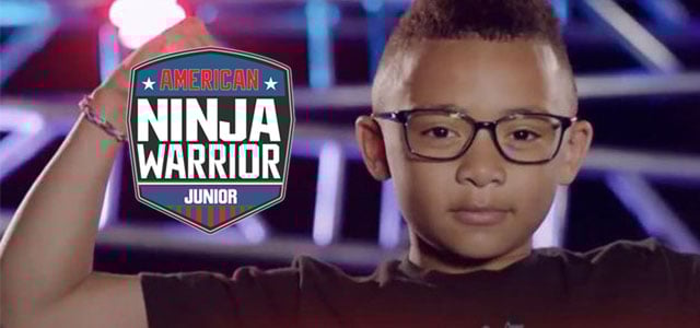 Large logo symbol of the TV show American Ninja Warrior Junior to the left of headshot of a determined looking young boy wearing glasses and with a spike-mohawk haircut