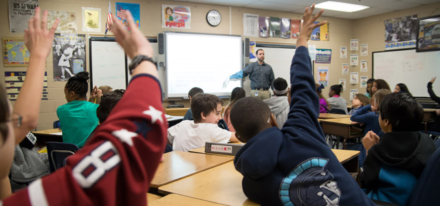 A classroom with a group fo students raising their hands