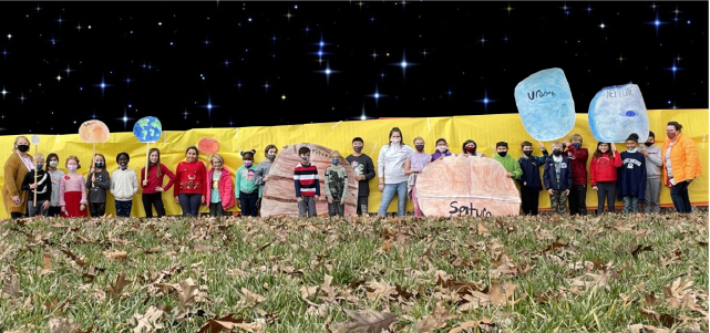 Students posing in front of school fence with planets they created