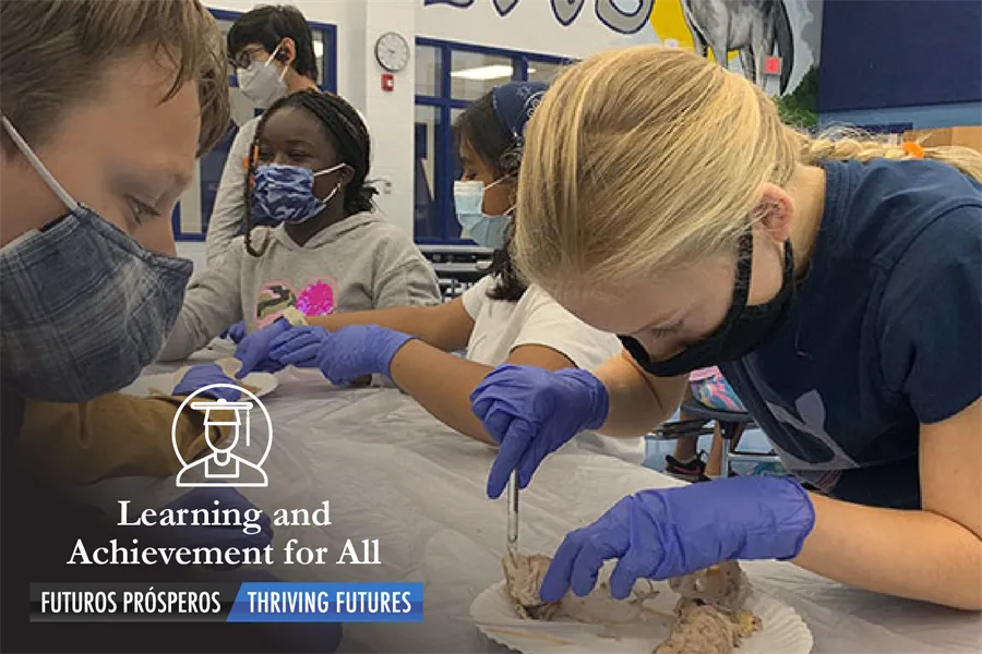 Several middle school students wearing face masks and purple surgical gloves facing the brain dissection science lab experiment, image bears the text Learning and Achievement for All, Aprendizaje y logros para todos (Spanish)