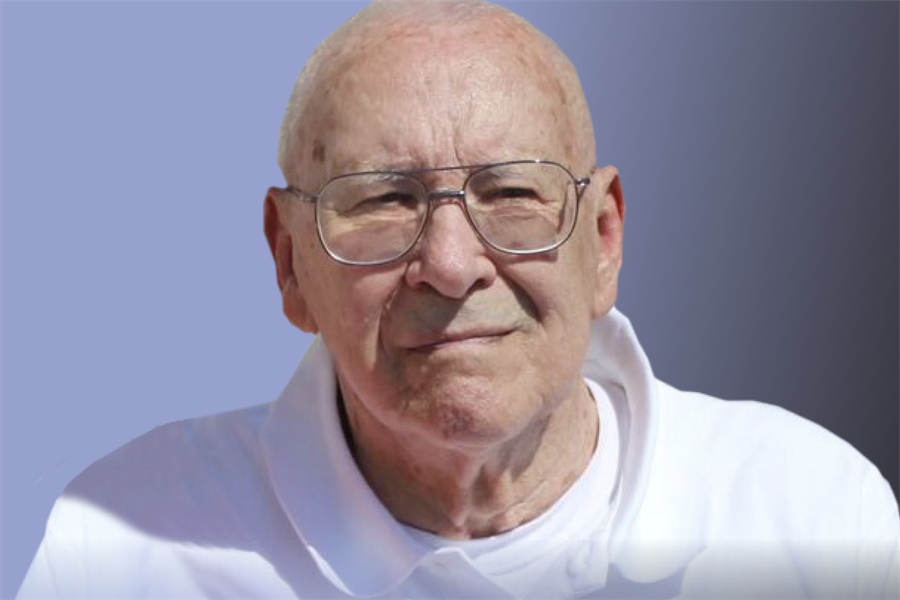 Close head photo image of a bald elderly man showing the collar of a white polo shirt and wearing wire-framed glasses squinting into the sunlight with a blue sky background