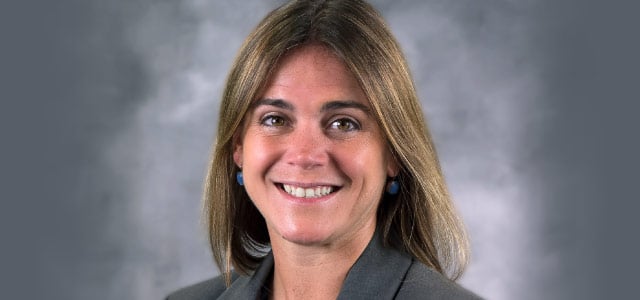 Smiling head-and-shoulder photo of Ashley E. Reyher, who has long light brown hair,  on a grey smokey background