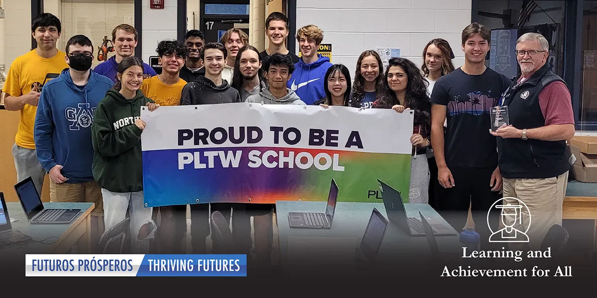 George Bishop pictured with students holding a sign that says "Proud to be a PLTW School"