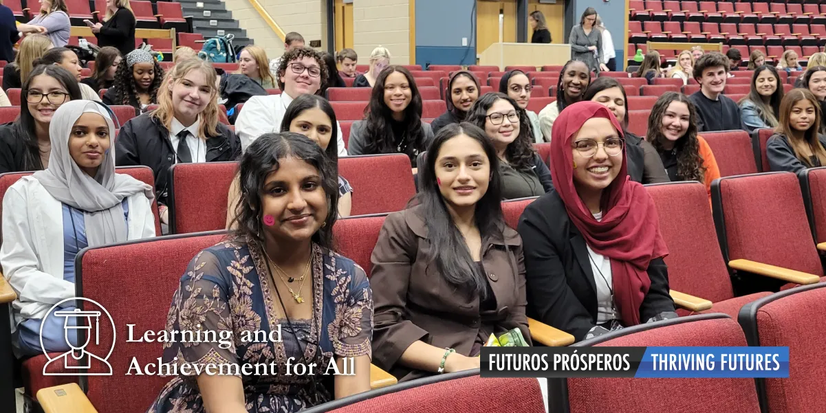 Smiling faces of about 50 students sitting together in red-upholstered auditorium seating with the text Learning and Achievement for All superimposed over the photo