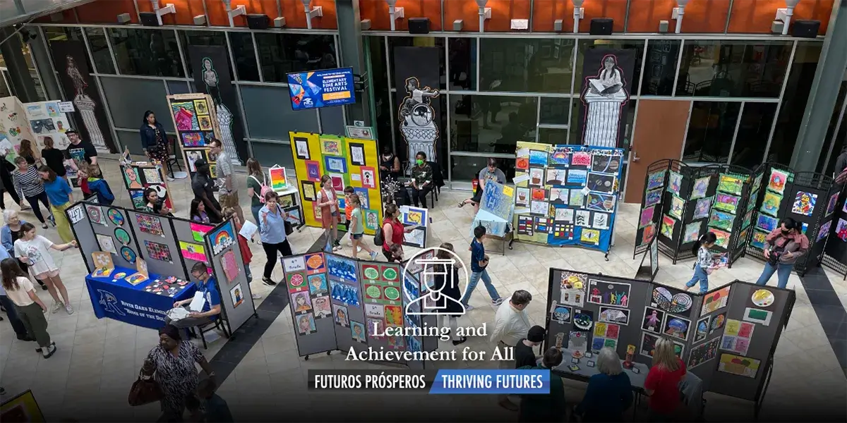 Aerial view looking down at the PWCS Kelly Leadership Center atrium from above with all the art displayed on tables and vertical stands and with visitors walking around viewing the pieces. The words Learning and Achievement for All superimposed over the image