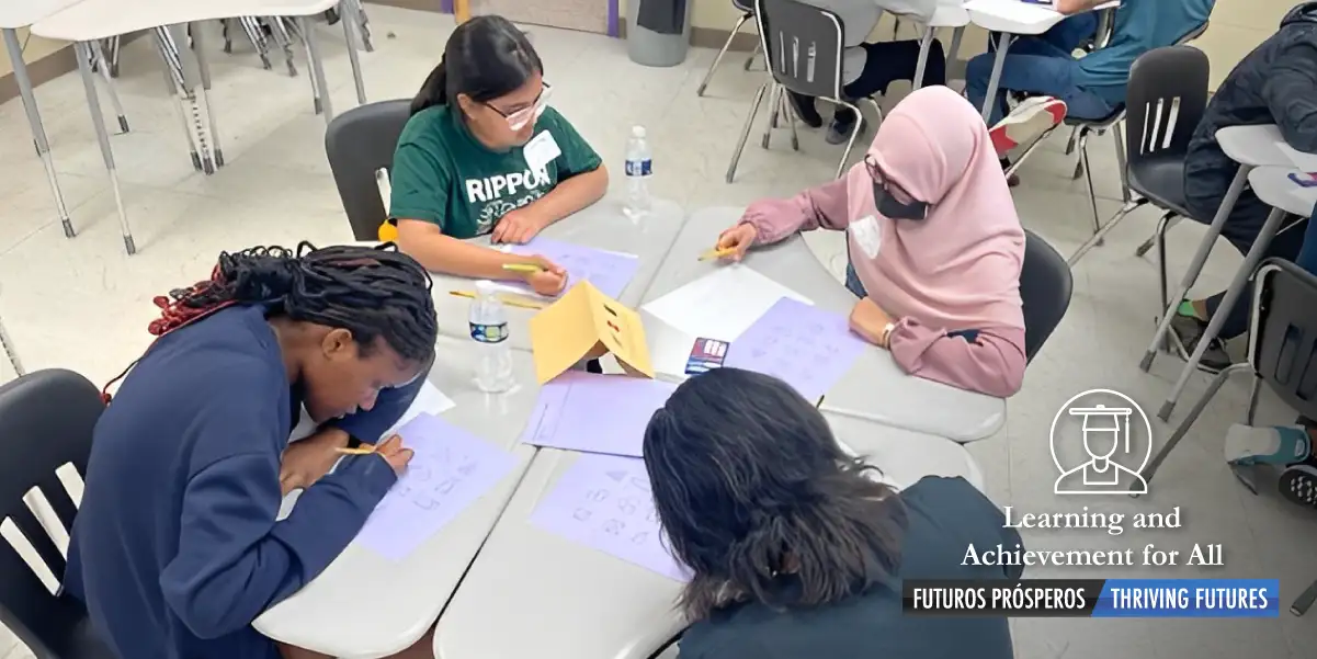 photo image of four students sitting at a round table and each is focused and working hard on the problems on the papers in front of them.