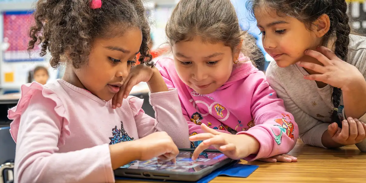 Three students at a table working on a tablet