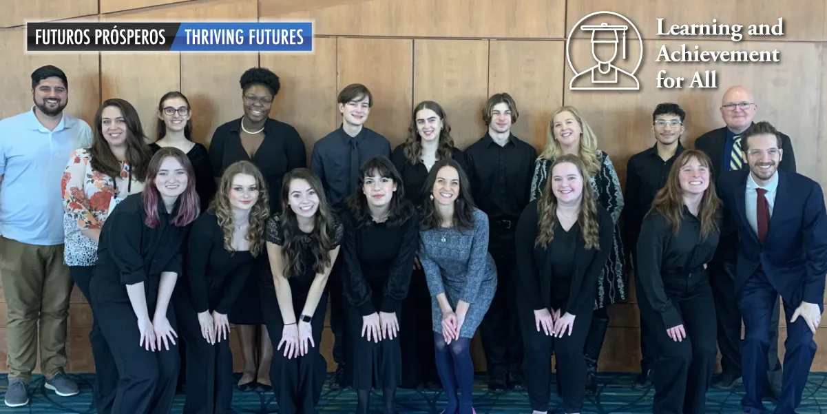 Photo image of a diverse group of about 15 smiling, professionally dressed high school students with a few adult educators standing in front of a panelled wall.