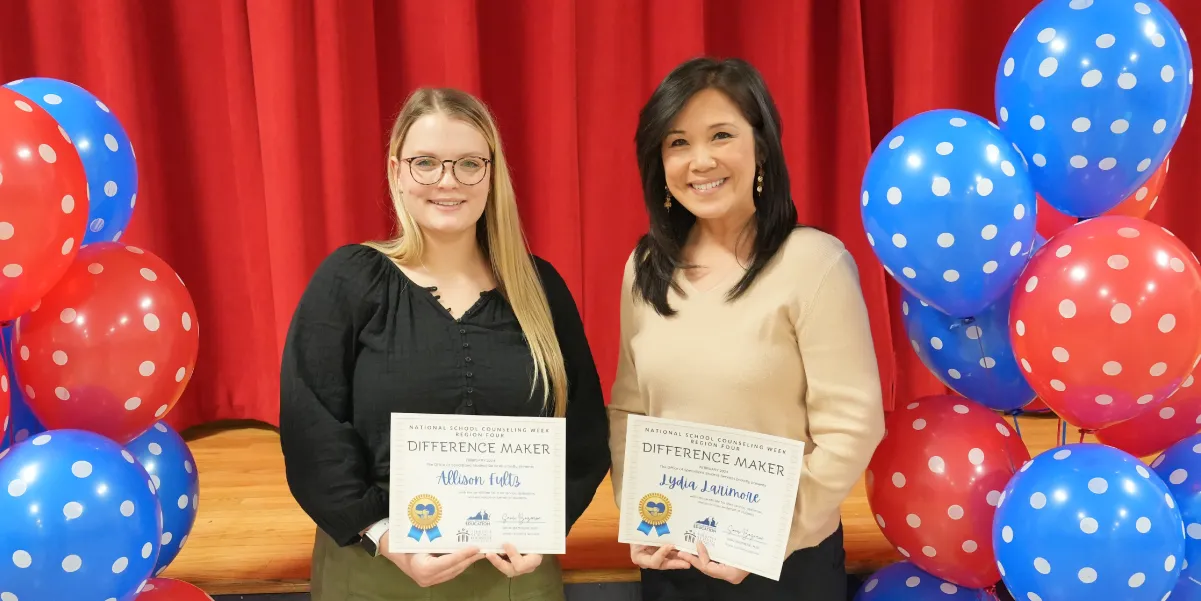 Two counselors with certificates standing in between balloons