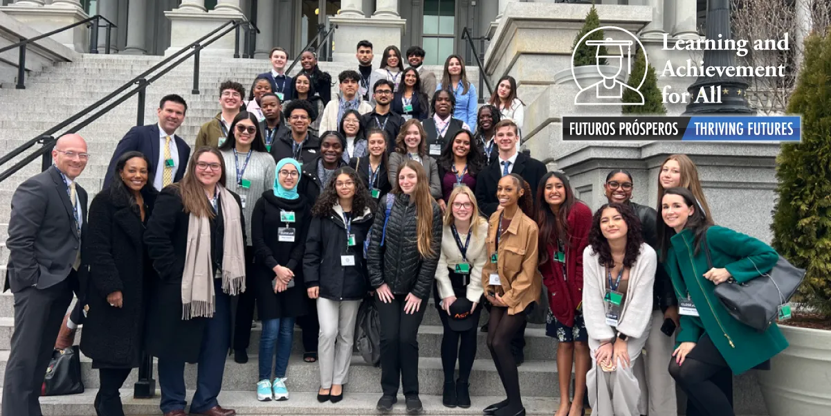 Photo of about 20 students with several adult school administrators or teachers some wearing coats and scarves, gathered in a group outside on the steps in front of a large government building. In the top right corner of the photo is the PWCS logo of the head of a graduate with a cap and the text Learning and Achievement for All, Futuros Prosperos, Thriving Futures